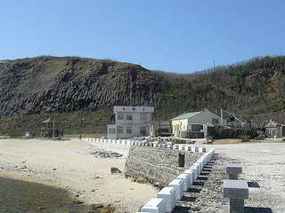 下了山，回到碼頭邊，鏡頭前方是東吉衛生所，偶有離島醫生或護士會來此短暫停留、看診。前方的沙灘一隅，就是粒粒皆清楚的閃亮貝殼沙（東吉老村長對這兒的沙質可驕傲的勒）～